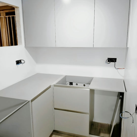 Montaje de cocina blanca en U con muebles sin tiradores, módulos bajos y conexiones pendientes de finalizar