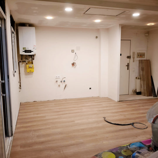 Espacio abierto antes de instalar una cocina con isla, con suelo efecto madera y conexiones preparadas
