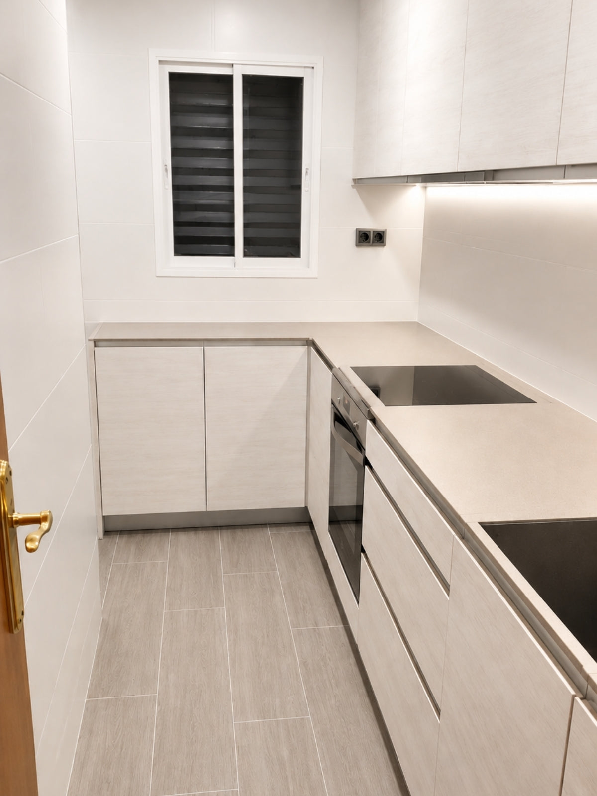 Cocina blanca compacta a medida con ventana y encimera clara en Badalona