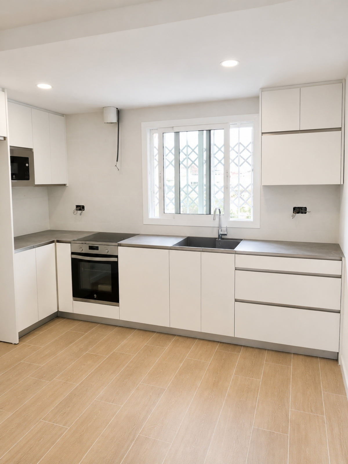 Cocina blanca en L a medida con ventana, horno integrado y encimera gris en El Masnou