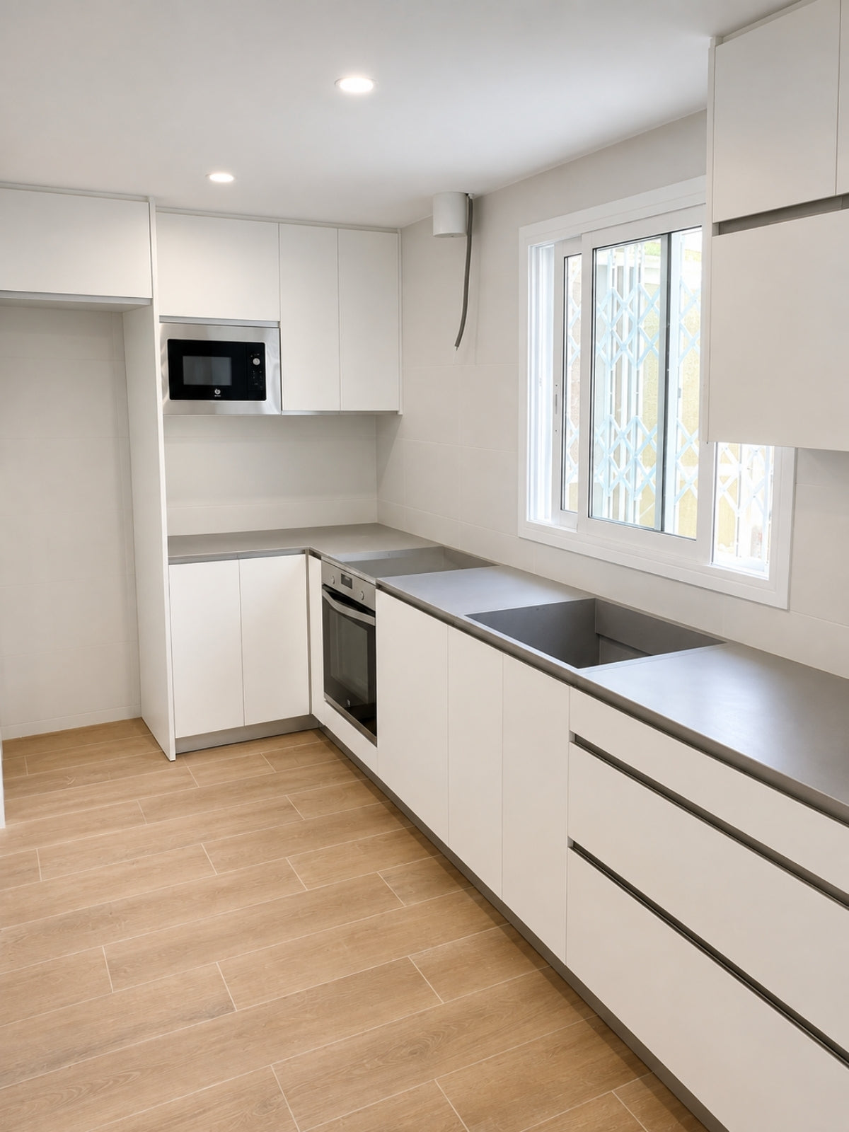 Cocina blanca en L a medida con ventana y encimera gris en Tiana