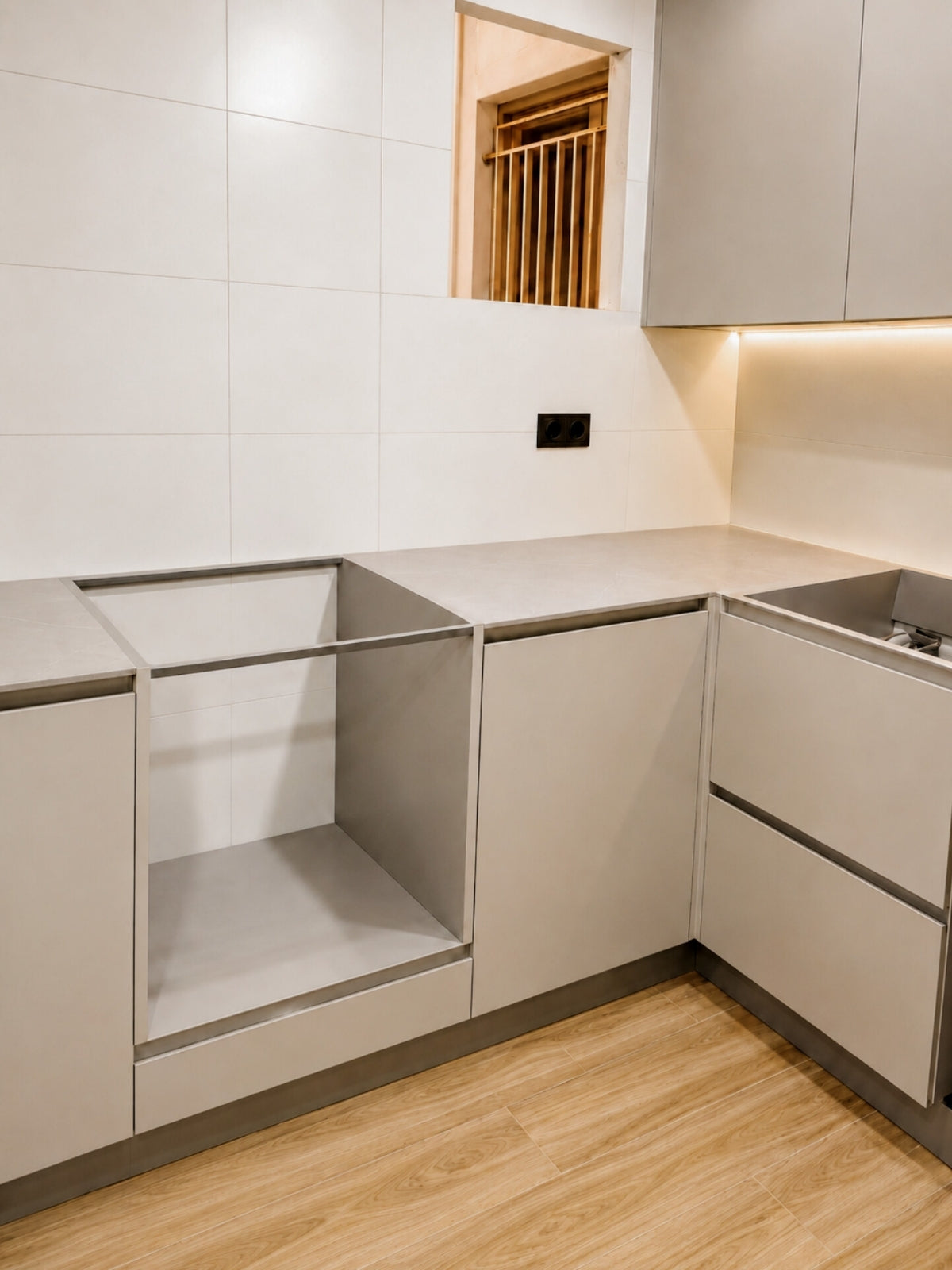 Cocina gris en L en Barcelona con muebles de frente liso, encimera clara, iluminación bajo mueble y suelo imitación madera.