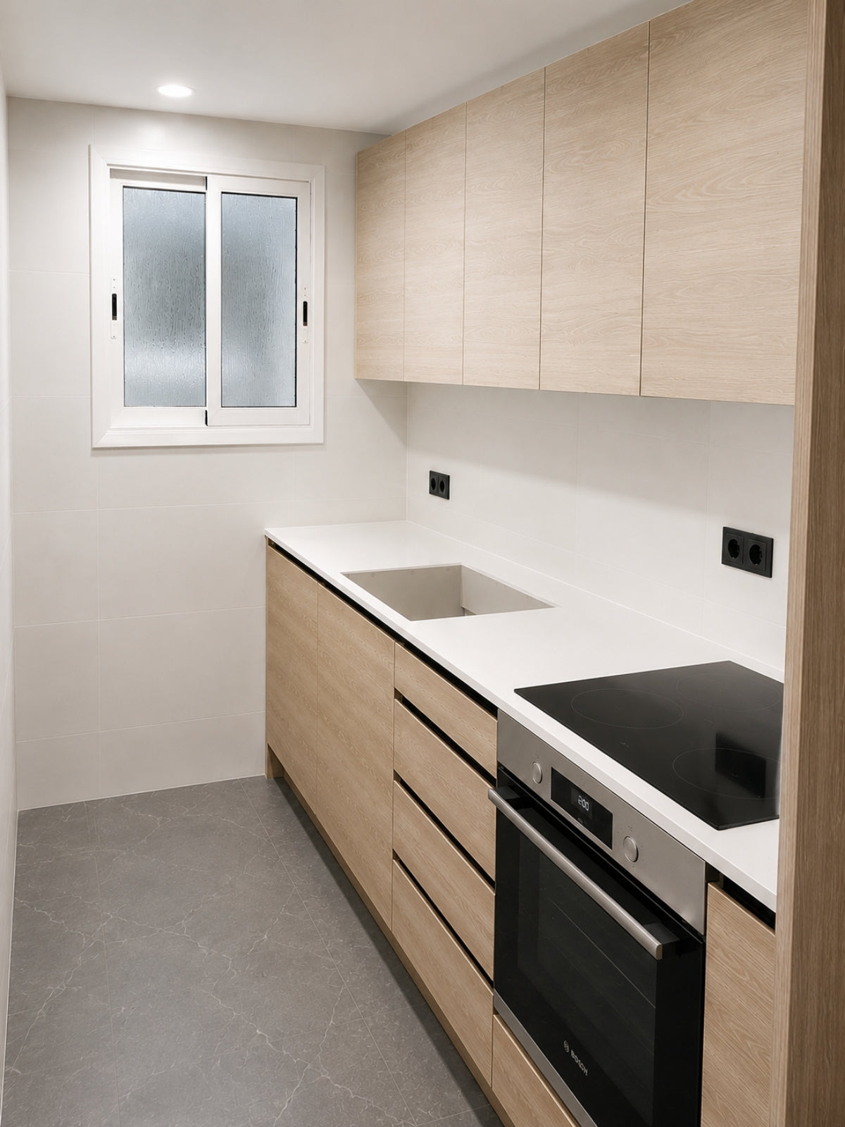 Cocina de madera clara a medida con muebles altos y ventana en Badalona