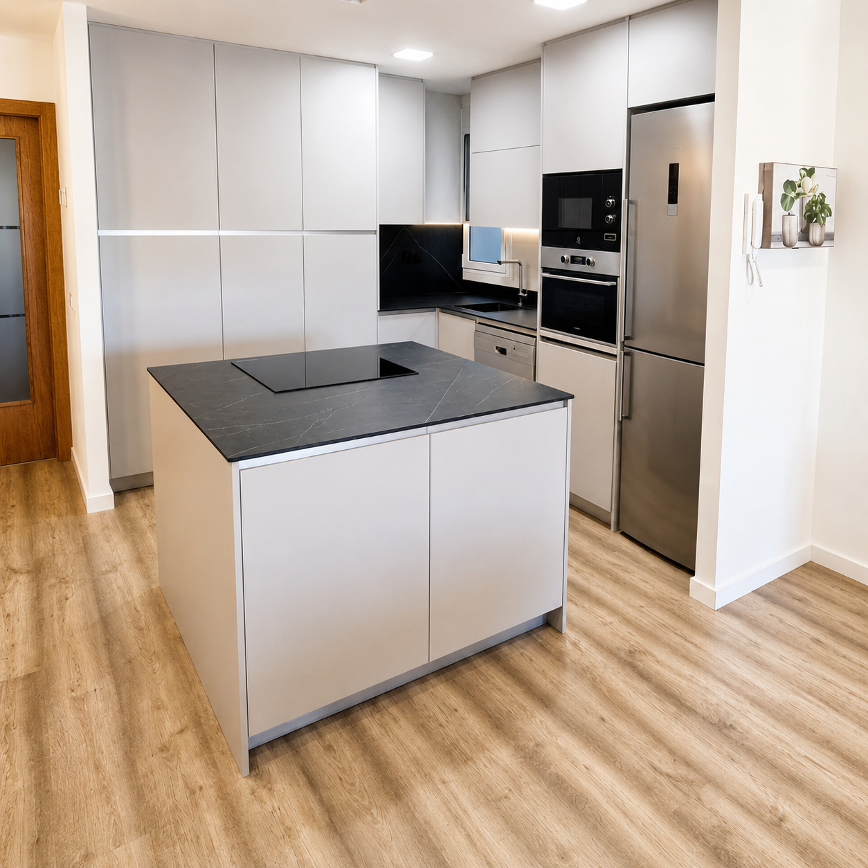 Cocina moderna con isla central, encimera oscura, muebles gris claro, columnas y electrodomésticos integrados
