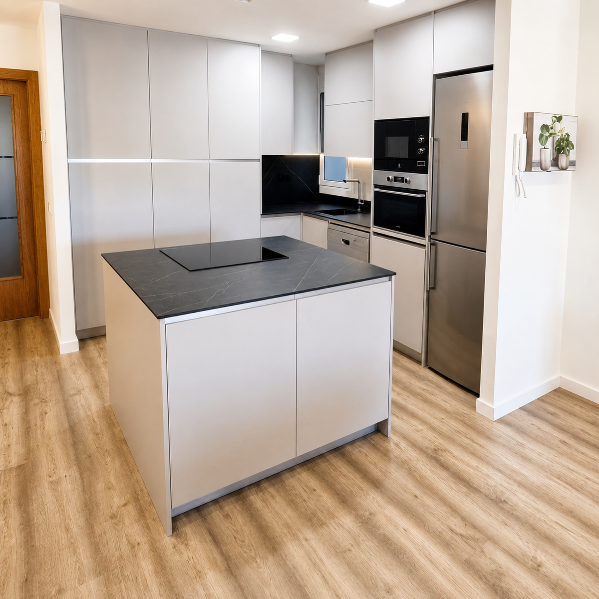 Cocina moderna con isla central, encimera oscura, muebles gris claro, columnas y electrodomésticos integrados