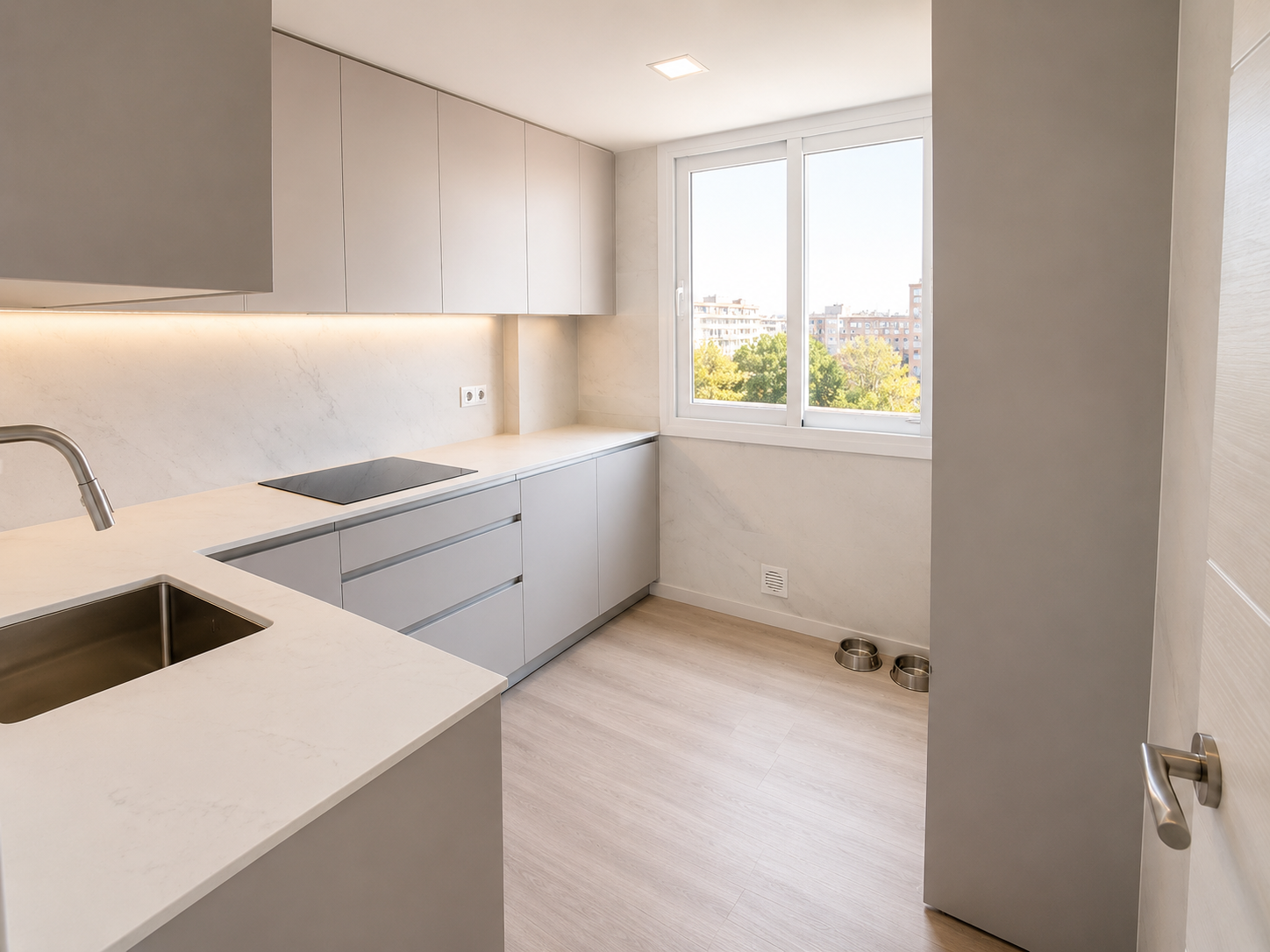 Cocina moderna en U con muebles gris claro, encimera blanca, fregadero, placa de inducción y gran ventana