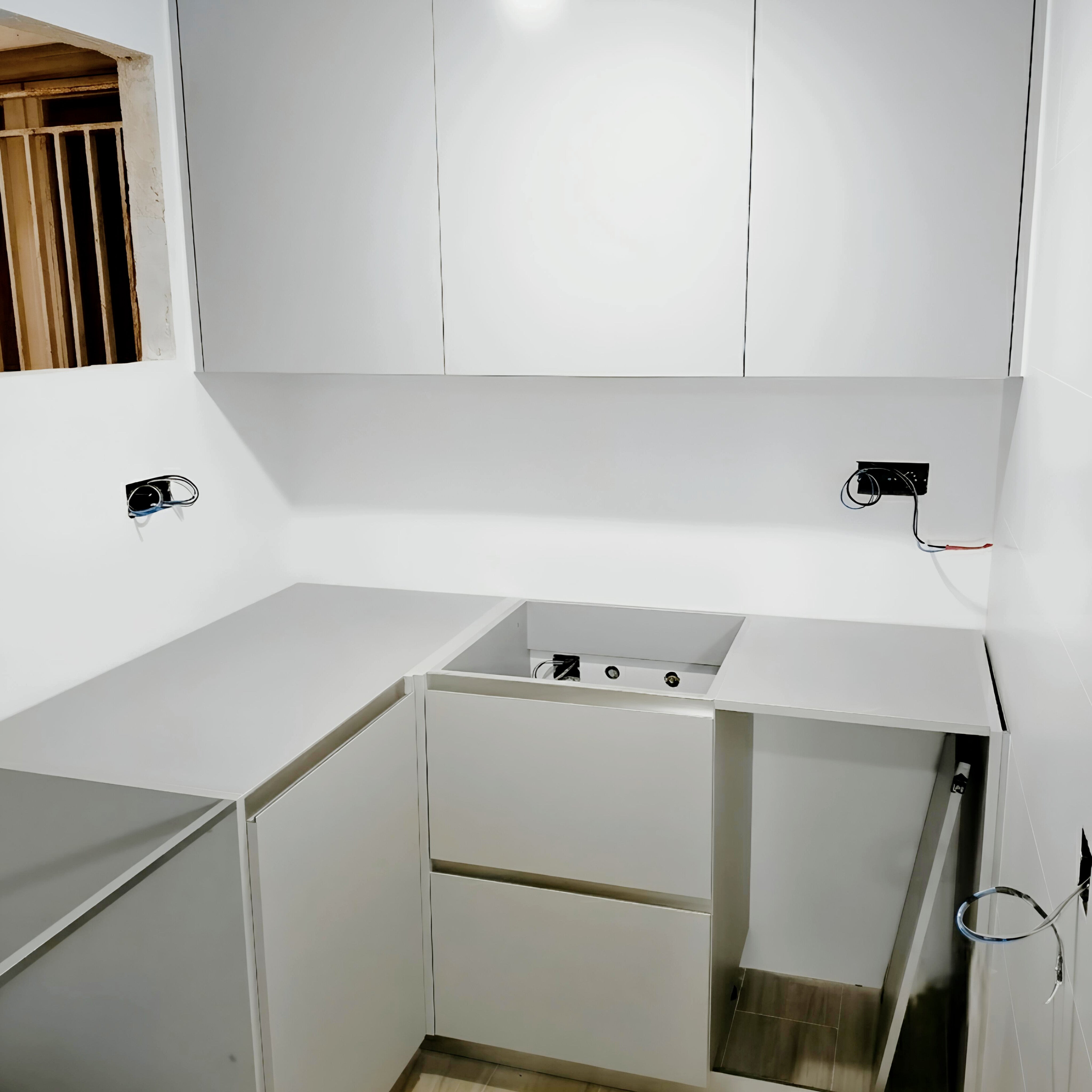 Montaje de cocina blanca en U con muebles sin tiradores, módulos bajos y conexiones pendientes de finalizar