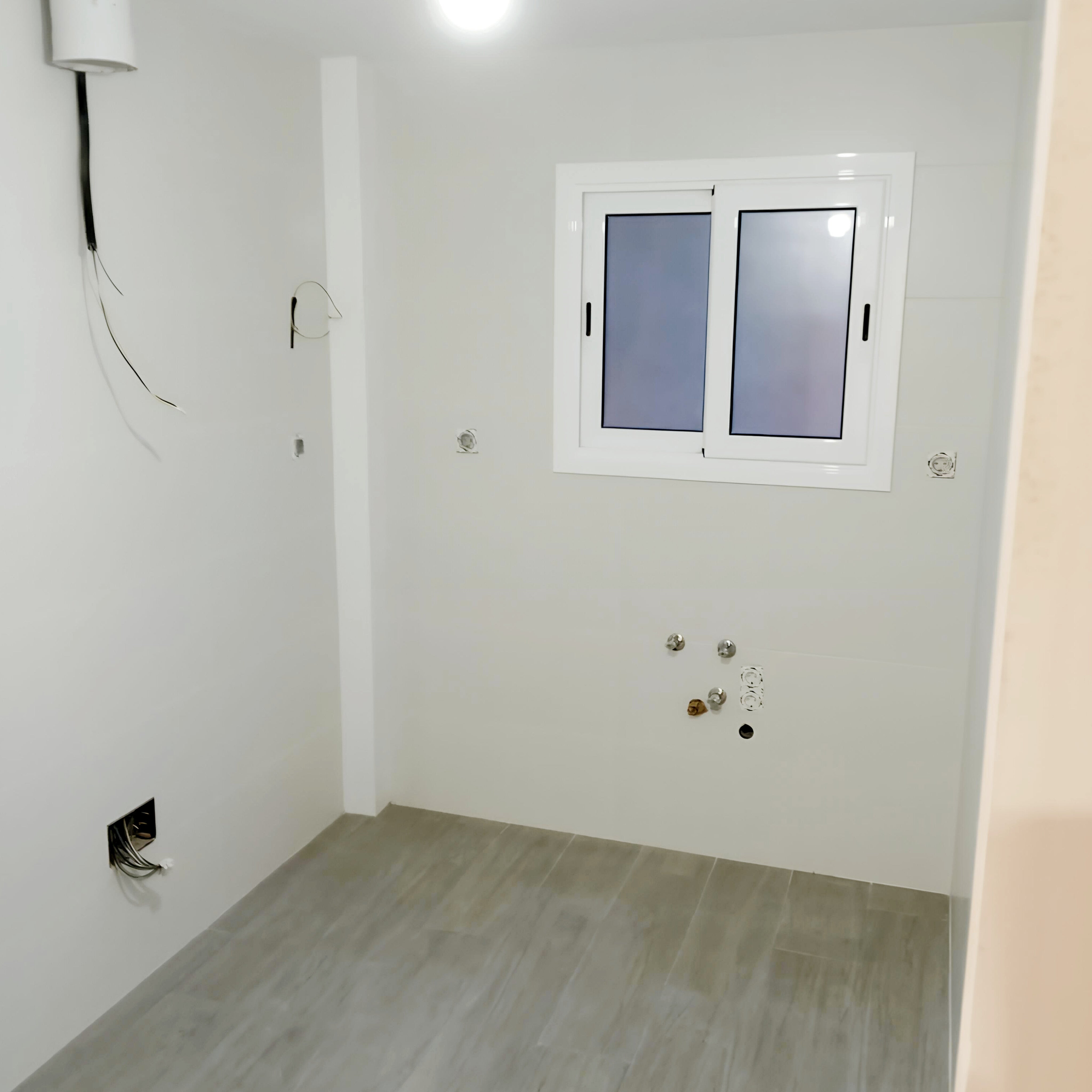 Espacio vacío antes de instalar una cocina en U, con ventana y conexiones de agua y electricidad preparadas