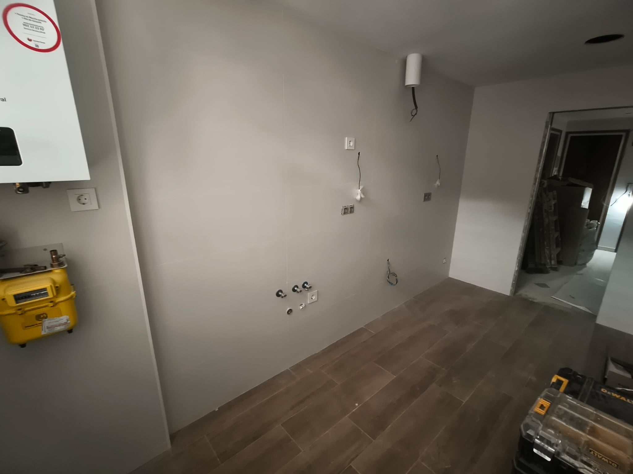 Espacio alargado antes de instalar una cocina lineal, con suelo efecto madera y conexiones de agua y electricidad preparadas