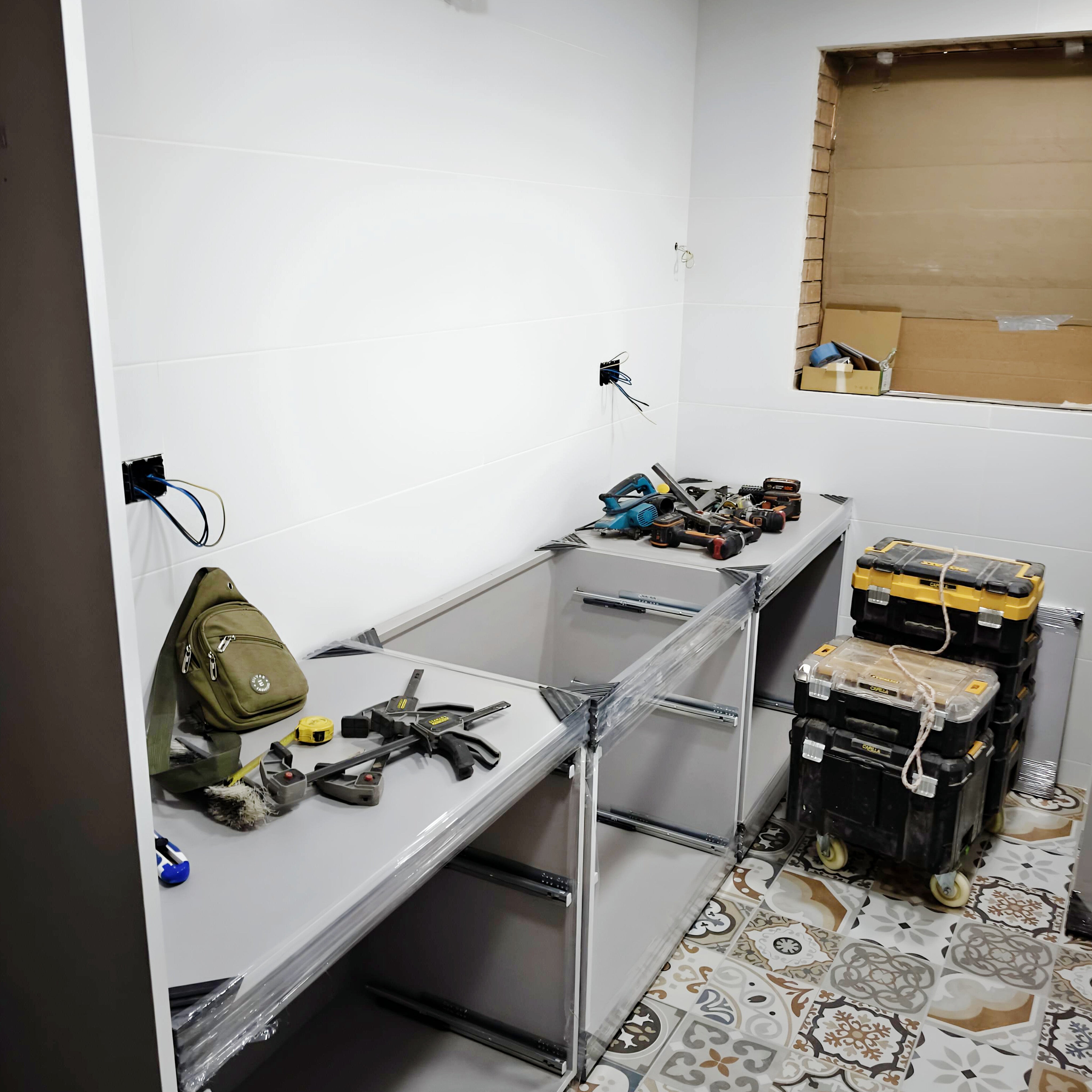 Montaje de cocina blanca con módulos abiertos, herramientas de instalación y suelo de baldosas hidráulicas