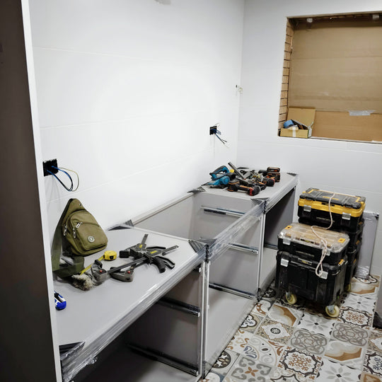 Montaje de cocina blanca con módulos abiertos, herramientas de instalación y suelo de baldosas hidráulicas