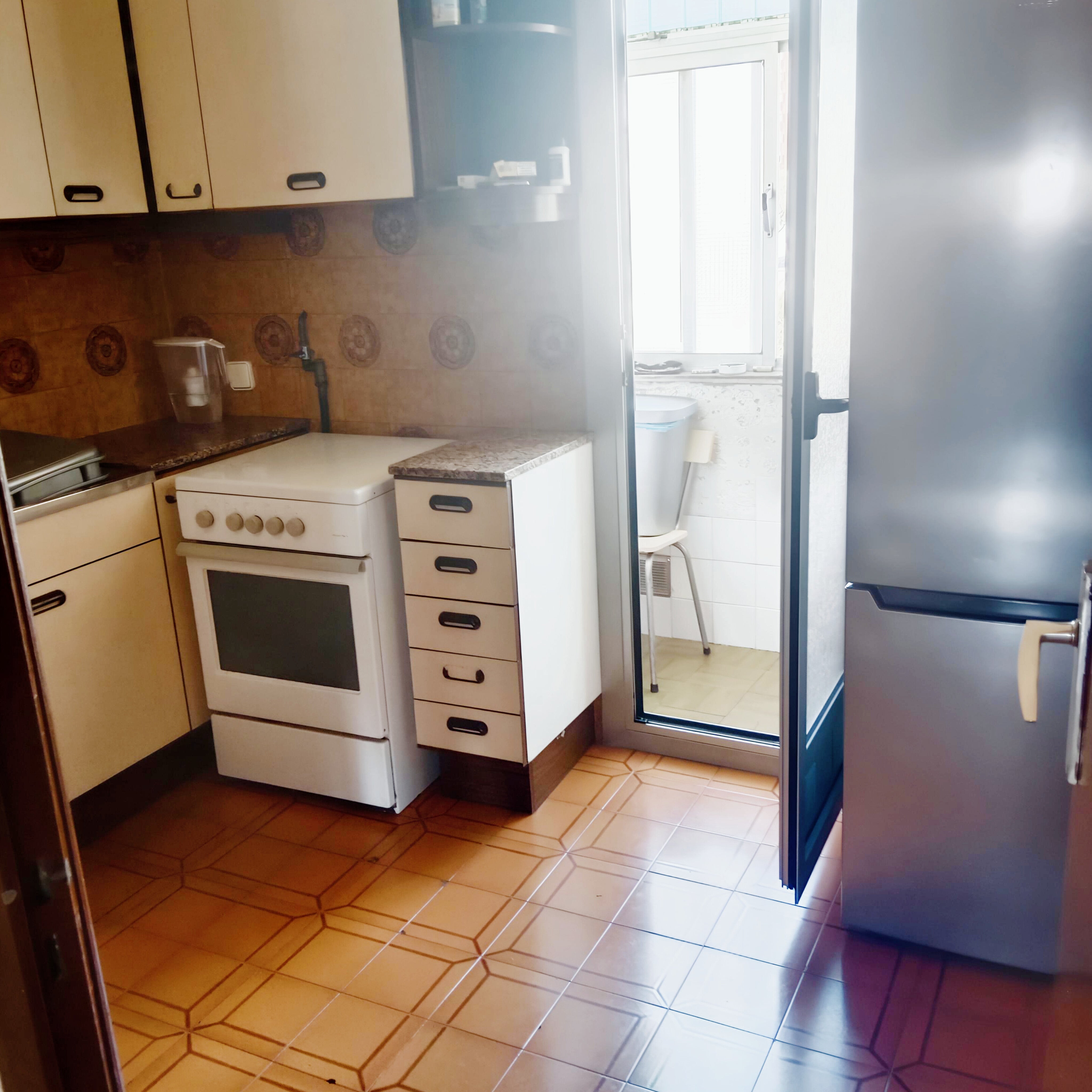 Cocina antigua y estrecha con muebles crema, cocina de gas, suelo marrón y acceso a galería